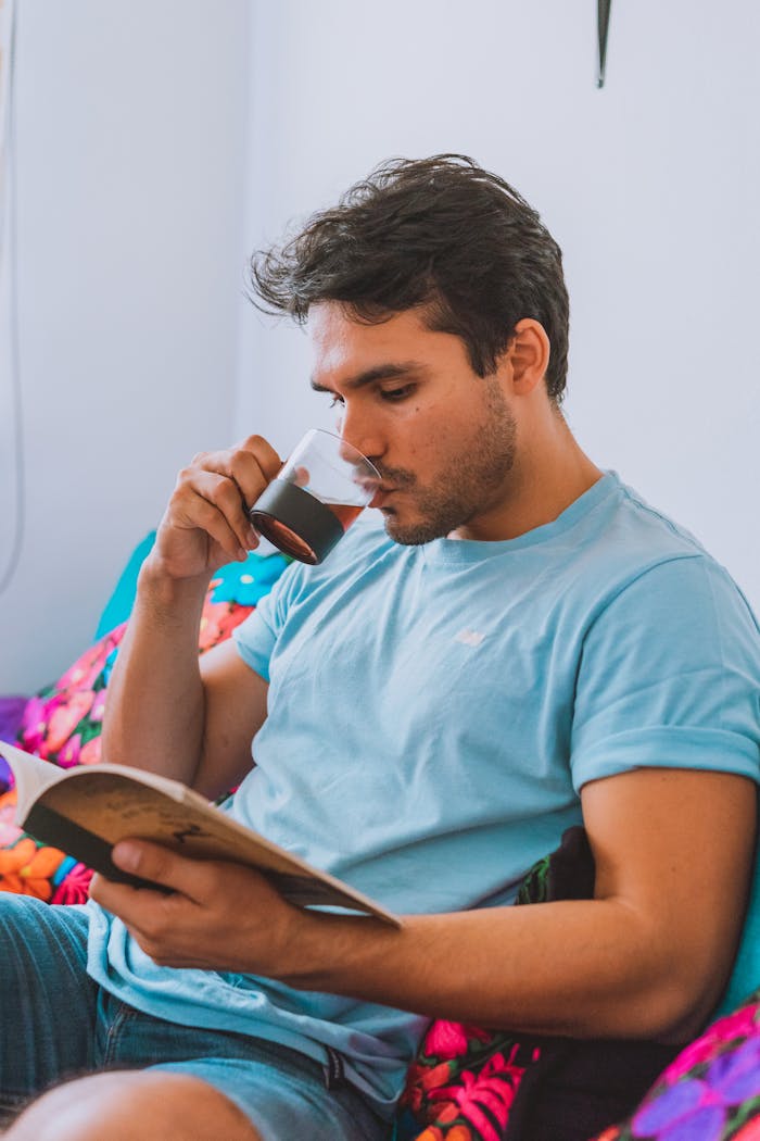 A man sipping coffee while reading a book in a cozy setting, promoting relaxation and leisure.